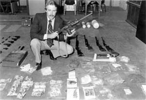 Man with gun standing over seized contraband - bags, money, guns