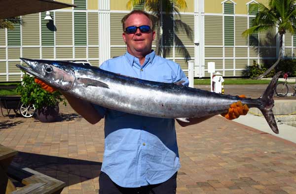 man holding a 40 pound wahoo fish in front of a marina