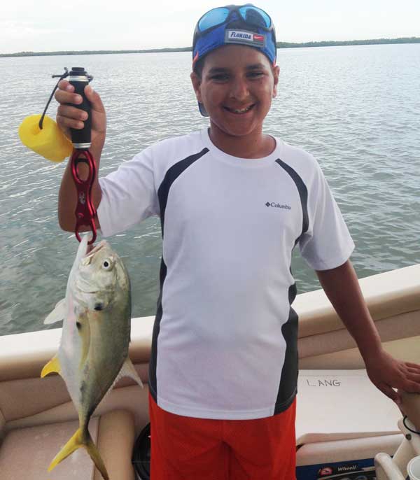 boy holds a crevalle jack with a lip grip on a boat