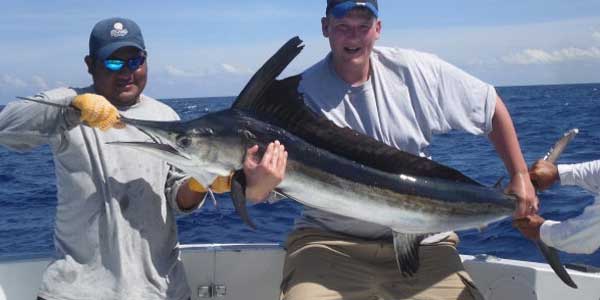 men on a boat holding a white marlin