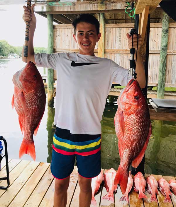 boy holding up 2 red snappers on a dock