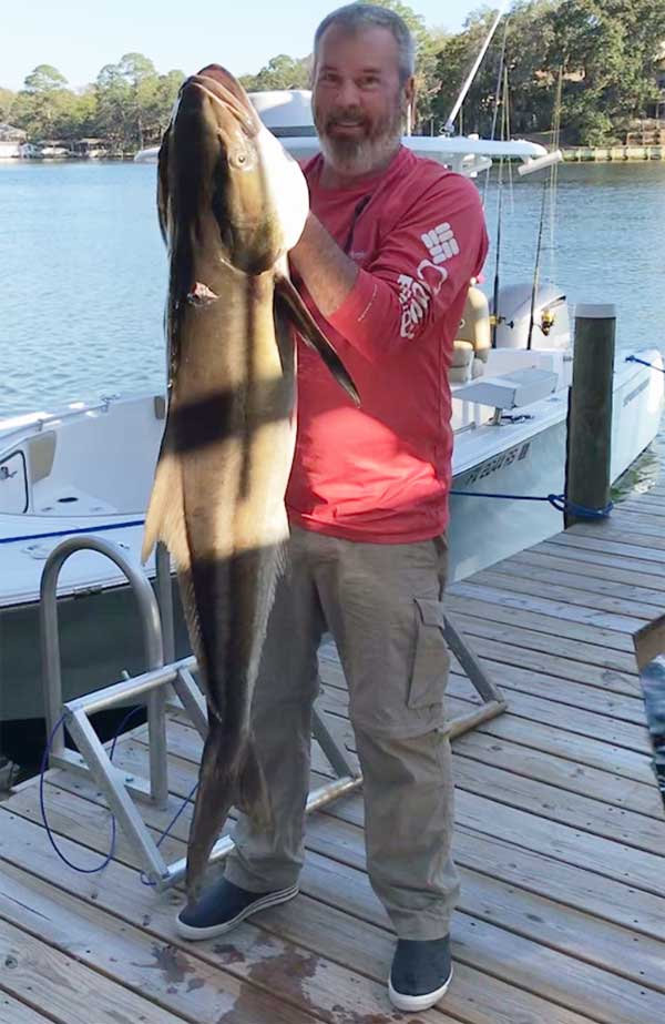 man holding a huge 48 pount Cobia fish on a dock
