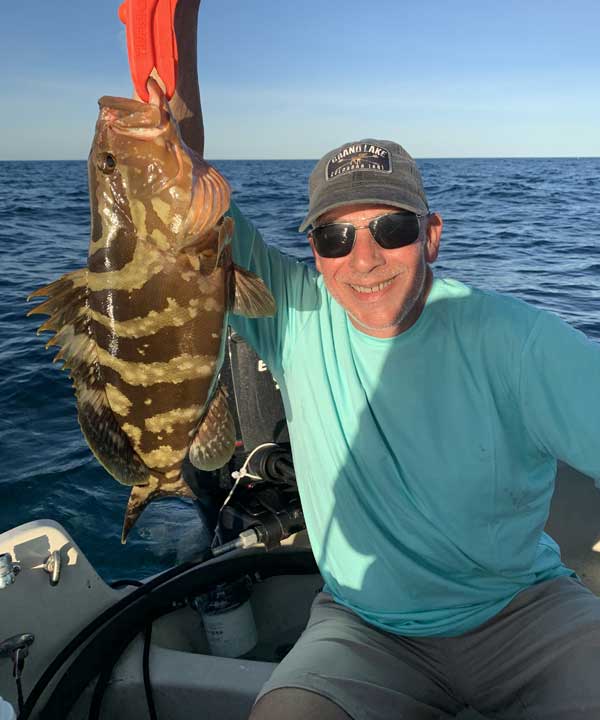 man on boat holding a nassau grouper from a orange lip grip