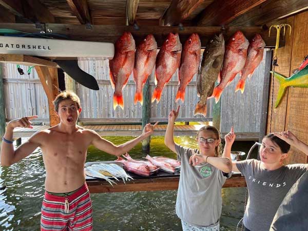 three kids on a dock pointing to their red snapper catch