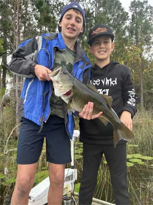 2 boys on a small boat on a lake holding a 10 lb large mouth bass