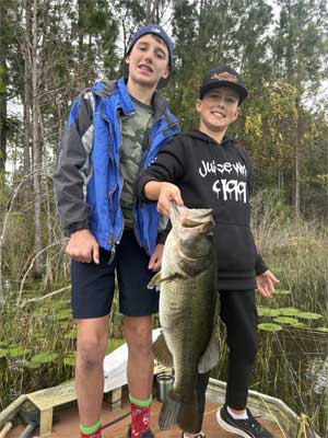 2 boys on a small boat on a lake holding a large mouth bass