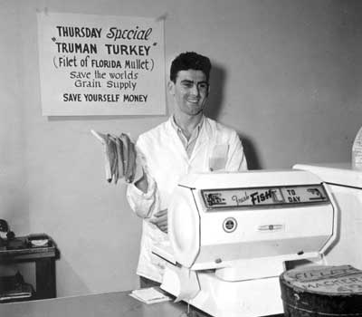 Man in butcher jacket at scale hold mullet fillets for sale