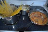 while fish is cooking in sauce cook pasta; notice alfredo sauce is ready in pan Pans with fish picatta, pasta in boiling water, cream sauce prepared