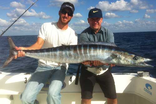 2 guys holding a huge Wahoo fish on a boat off miami