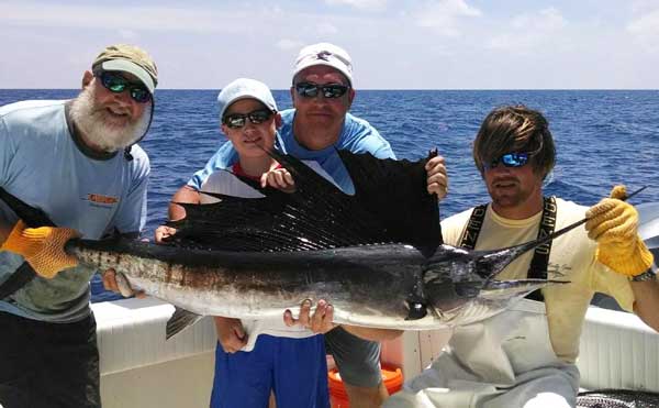 men and a boy holding up a sailfish on a boat in naples