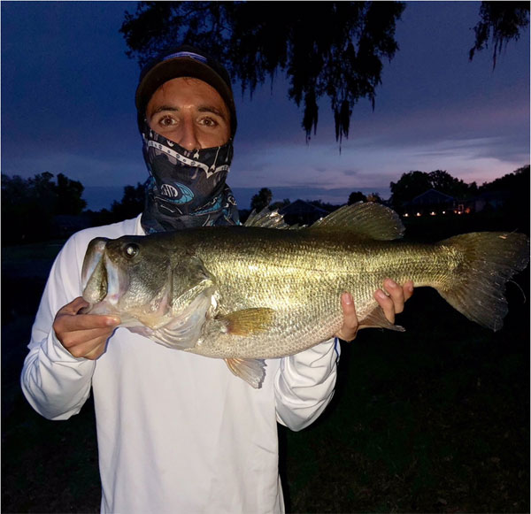 man with a sun rag on face holding a 10 pound bass at sunset