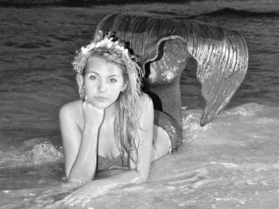 woman mermaid with long black hair surrounded by mangrove branches at the edge of the water