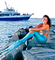 miss mermaid on the rocks looking at a huge passenger ship on the water