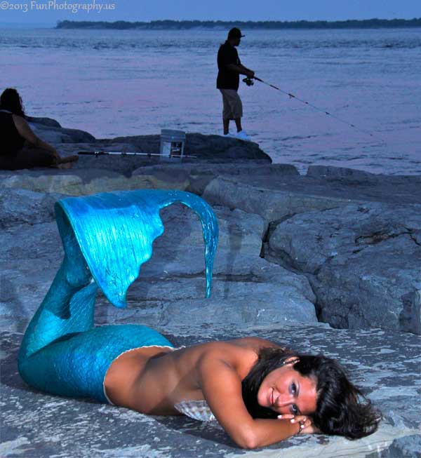 Mermaid on rock jetty with anglers fishing in the background
