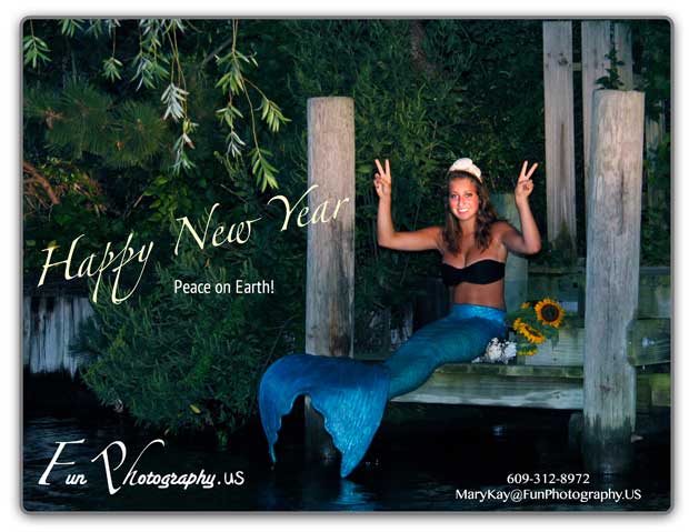 girl in mermaid costume sitting on dock with both hands held up with peace sign