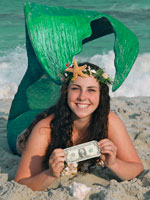 miss mermaid laying in the sand with a dollar bill
