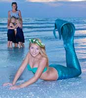 Mermaid on the beach with a mother and two girls looking on in the background
